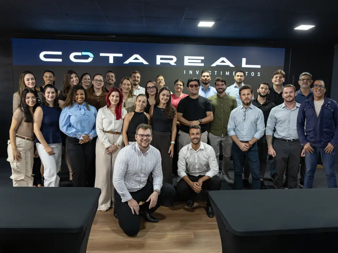 Equipe da Cota Real Investimentos reunida diante do letreiro da empresa