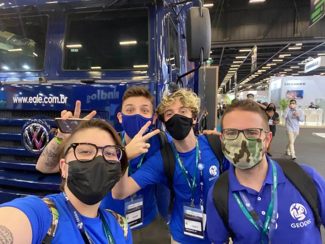 Enzo e três colegas da GEODIS, de máscara, em frente a um caminhão azul em um evento do setor