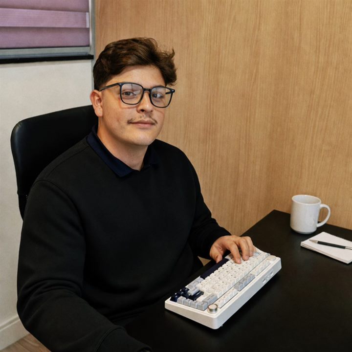 Retrato de Enzo Maziviero sentado à mesa, com um teclado mecânico à frente